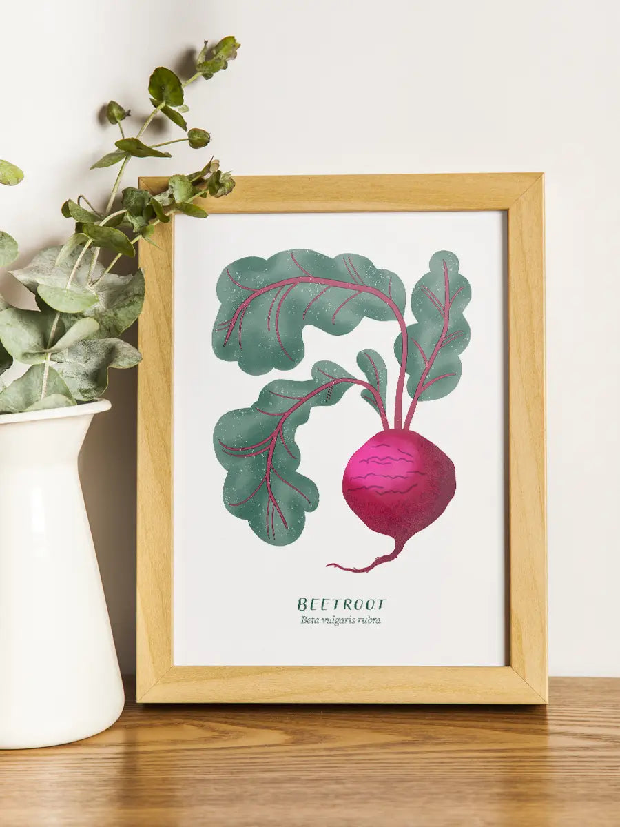 Framed artwork of a beet with lush green leaves on a wooden surface.