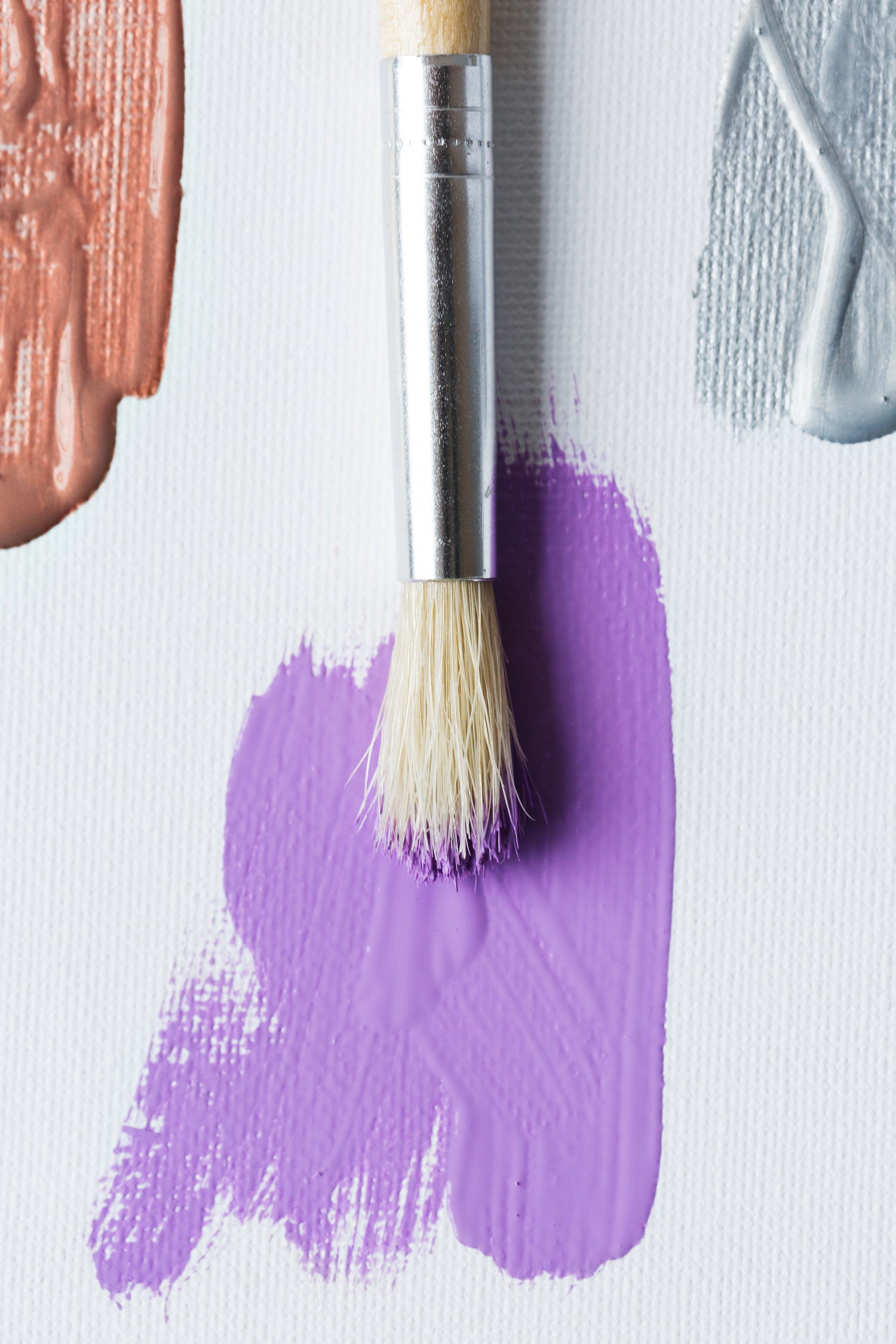 Closeup of paintbrush over a purple splotch of paint